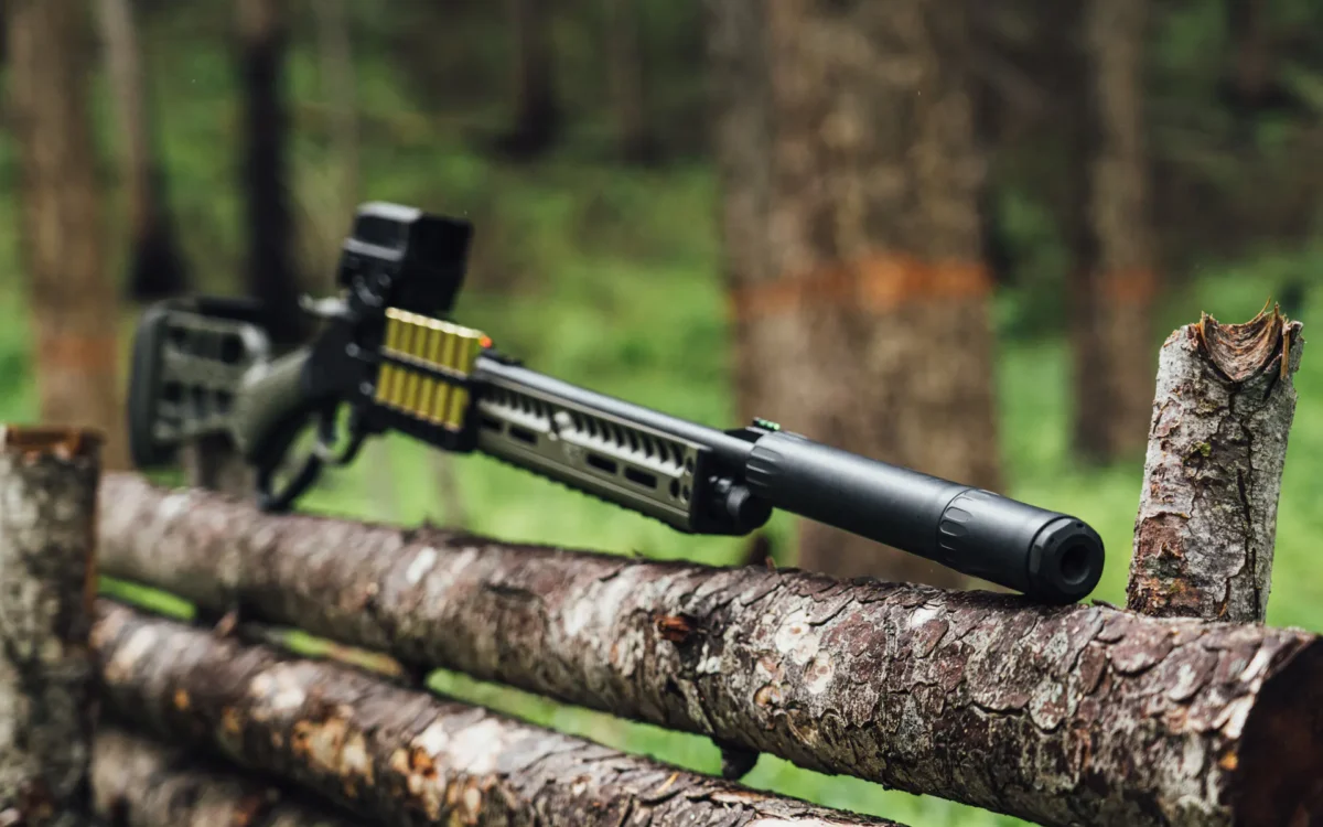 Suppressed shotgun resting on wooden fence outdoors